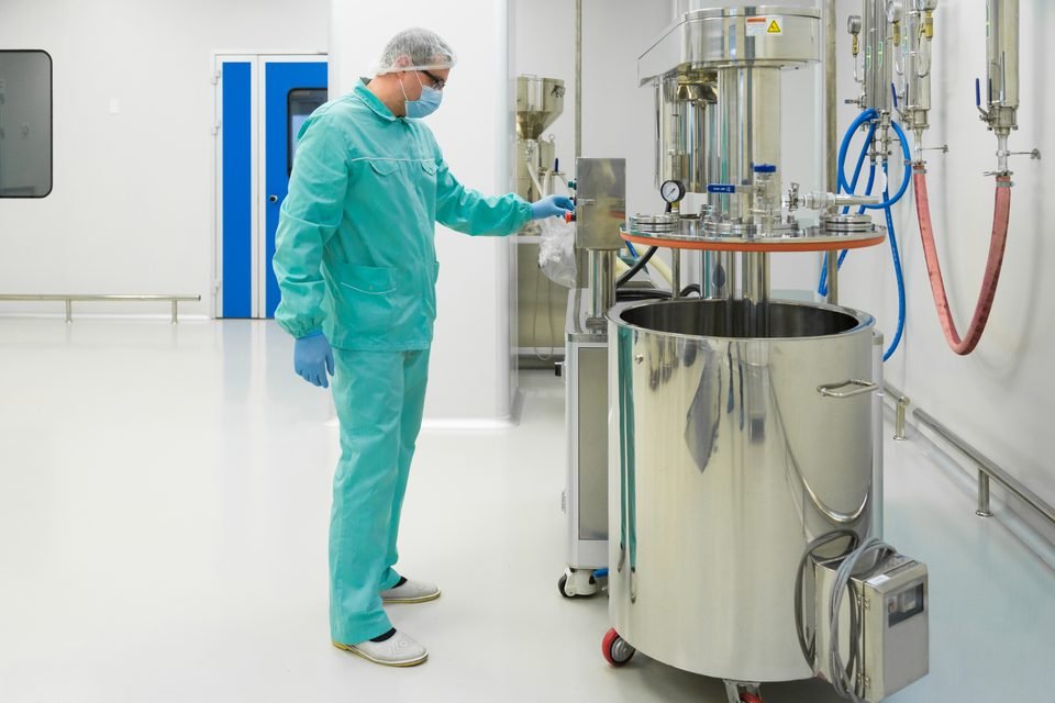 Gowned operator working at a sterile manufacturing vessel under cGMP conditions